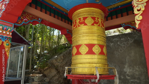 Fotografía Golden prayer wheel under ornate Tibetan structure with red and gold accents aga