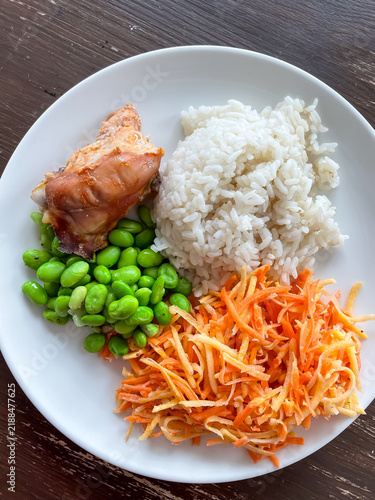 Top view of plate with balanced meal of rice, chicken, carrot salad and edamame, healthy eating and nutrition