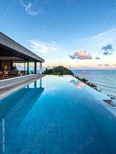 Luxurious modern villa with an infinity pool offering breathtaking ocean views under a clear blue sky.
