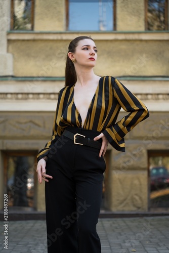 Portrait of an attractive young caucasian woman wearing a yellow and black striped blouse near a building. Fashion, style, beauty.