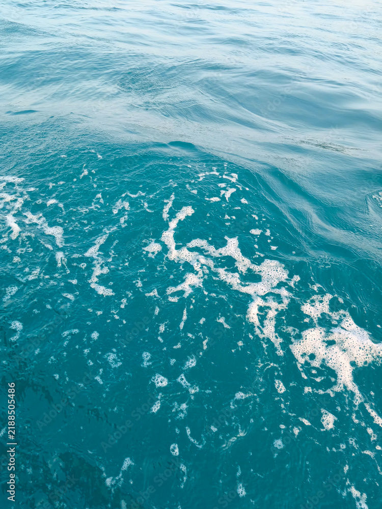 Fototapeta premium Texture of clear blue sea water ripples with white foam from boat waves