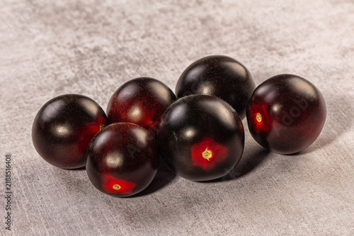 Canvas Print Dark purple cherry tomatoes with red undertones arranged on textured gray surfac
