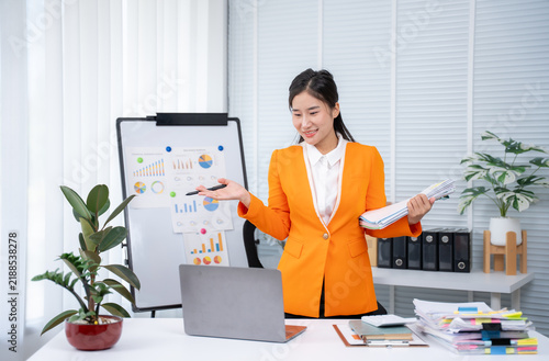 Fotografía Presentation Success: An elegant businesswoman delivers a compelling presentation, confidently gesturing towards charts on a whiteboard while holding documents