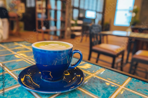 Foto A cup of green tea matcha latte with latte art served in a blue ceramic cup and saucer on a blue mosaic tiled table inside a cozy cafe with warm blurred background lighting for your morning ritual