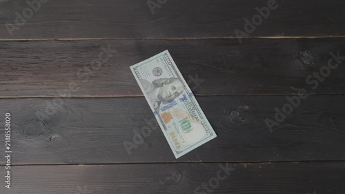 A USA dollar 100 bill lies on a dark wooden table, while numerous Chinese 100 yuan banknotes rain down upon it. A concept representing global economic competition and trade wars.