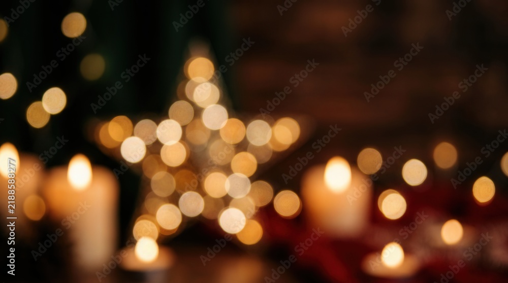 Fototapeta premium Christmas lights blur into soft golden bokeh circles surrounding glowing candles in the dark.