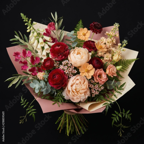 Beautiful mixed flower bouquet with red roses, pink peonies and greenery wrapped in paper on black background