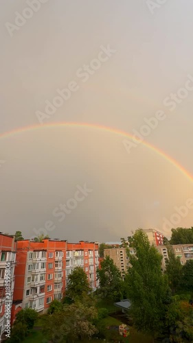 Beautiful double rainbow arching over a city residential area against a dramatic cloudy sky after rain