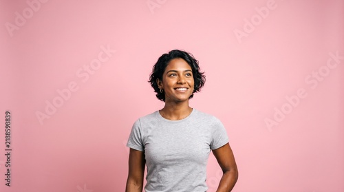 Smiling Indian woman with short dark hair wearing a grey t-shirt against a pink background