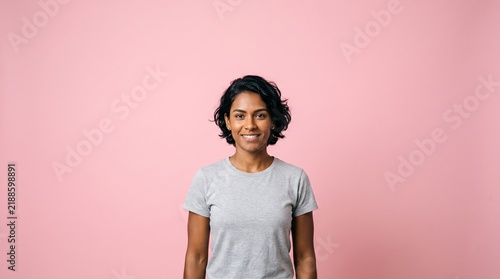 A young Indian woman with short dark hair smiles confidently against a plain pink background wearing a grey t-shirt