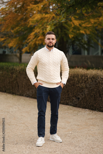 Taking a moment to relax outdoors, a casually dressed man sits comfortably in a stylish vest surrounded by autumn foliage. The cozy setting, natural light and warm colors create a calm seasonal atmosp