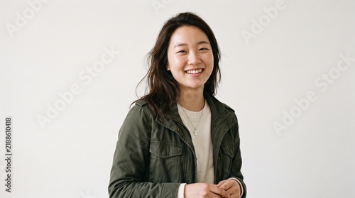 Portrait of Smiling Asian Woman in Green Jacket Against White Wall