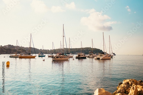 Sailboats and motorboats moored in calm Mediterranean waters along the waterfront in Menton, France. Warm sunlight illuminates the French Riviera coastline in September 2026.