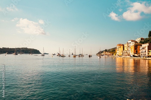 Sailboats and motorboats moored in calm Mediterranean waters along the waterfront in Menton, France. Warm sunlight illuminates the French Riviera coastline in September 2026.