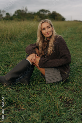 An attractive blonde woman is sitting in an autumn meadow in the countryside.
