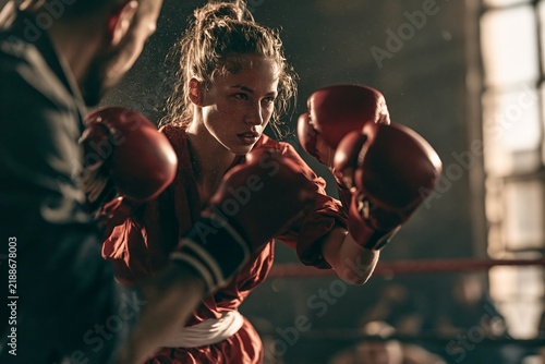 Focused young female boxer throwing punches with coach during intense training session in the ring