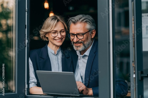 Smiling mature business couple working together on a laptop while sitting by a window in a cafe