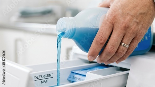Hand pouring blue liquid detergent into washing machine drawer