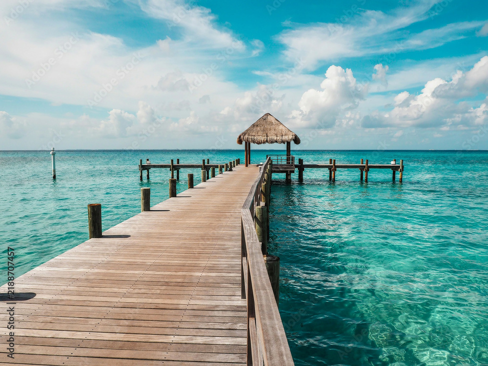 Obraz premium Wooden Pier Leading to a Thatched Hut Over Turquoise Tropical Waters