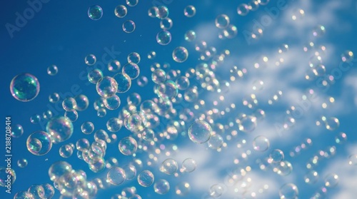 Many iridescent bubbles floating against a bright blue sky with clouds