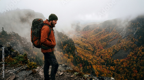 Male hiker with heavy backpack standing on a foggy mountain ridge overlooking an autumn valley with colorful fall foliage, adventurous trekking and wilderness exploration in misty nature Generative Ai