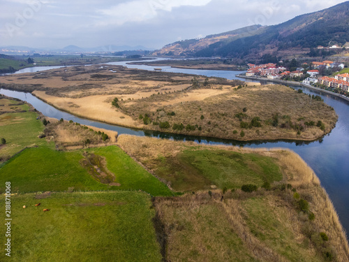 Aerial view of the Asón River estuary surrounded by lush green fields and rolling hills near the town of Limpias. Cantabria, Spain.