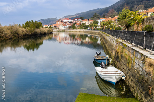 Asón River reflecting clouds, featuring a boat pier and a promenade lined with palm trees in Limpias. Cantabria, Spain.