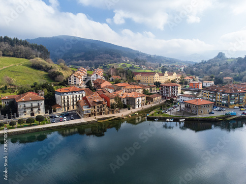 Aerial view of the Asón River with cloud reflections, the town of Limpias and its promenade, surrounded by green fields and hills. Limpias, Cantabria, Spain.