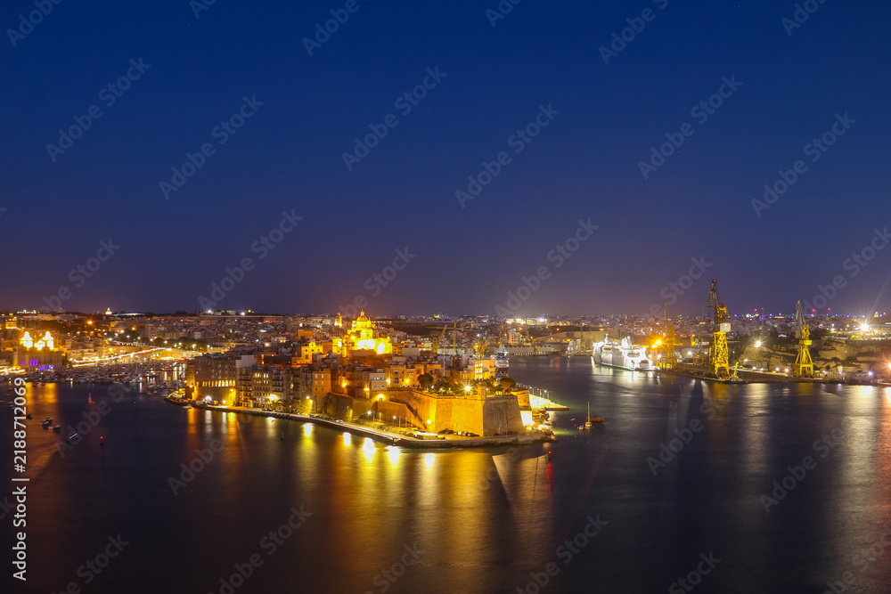 Fototapeta premium Night view of Fort St. Angelo and Birgu town illuminated over the Grand Harbour from the Upper Barrakka Gardens in Valletta, Malta