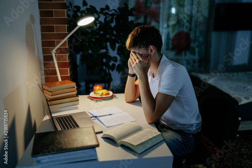 Stressed teenage schoolboy covering his face failing a difficult night homework.