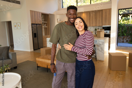Diverse couple standing in open-plan kitchen holding keys and unpacking cardboard boxes