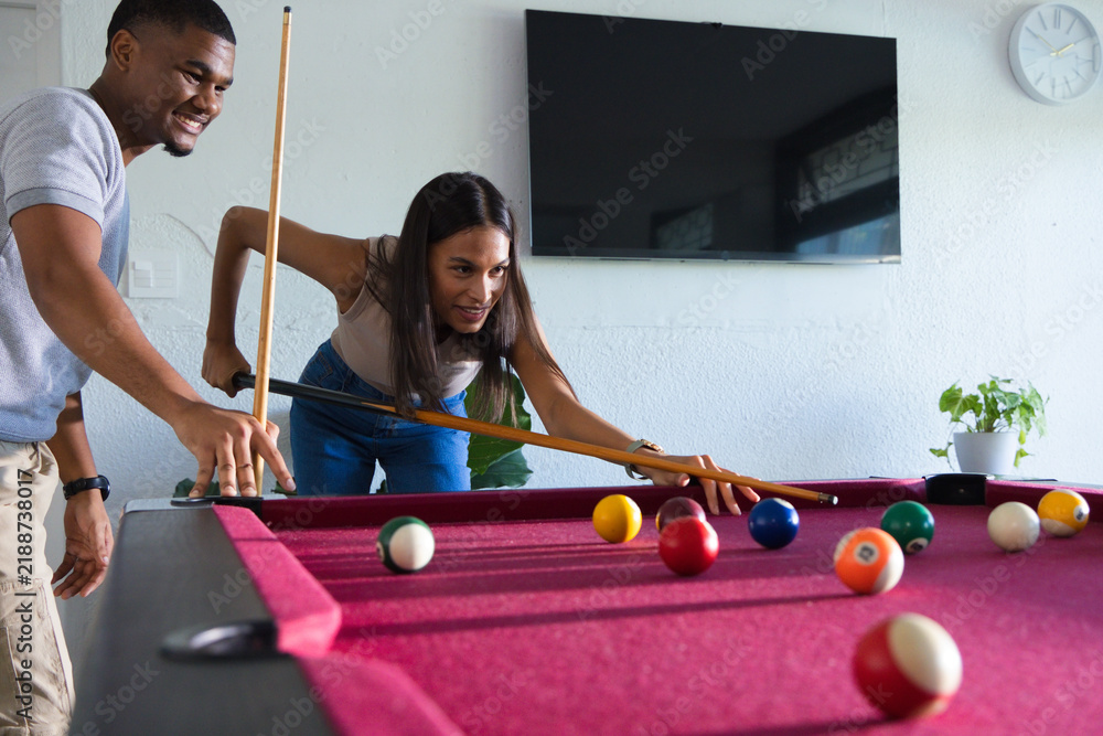 Fototapeta premium African American couple playing pool in game room, woman leaning, holding cue, balls on table