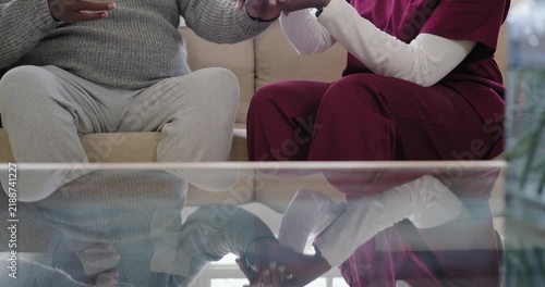 African American caregiver in scrubs testing man's wrist on sofa via glass while he explaining pain