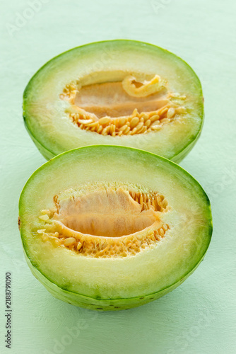 Two halves of unripe Charentais melon -  the best substitute for green papaya in Thai Som Tam salad. Pastel green background.