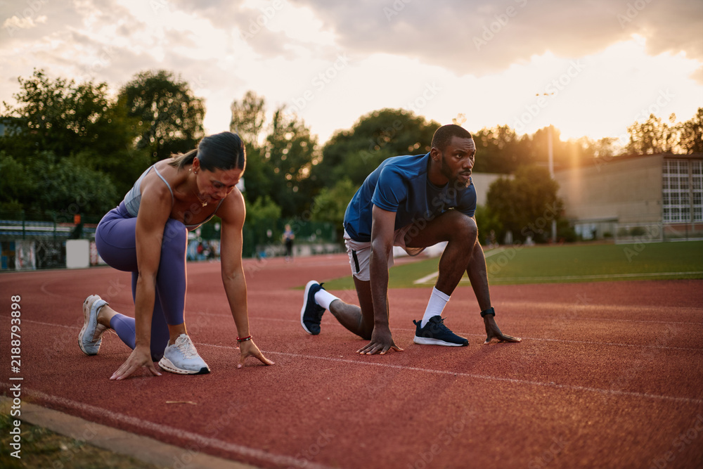Fototapeta premium Athletes starting a race on running track at sunset
