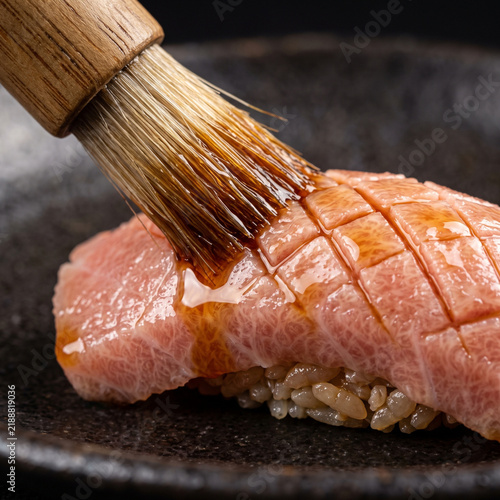 Chef brushing savory nikiri soy sauce onto scored fatty otoro tuna nigiri sushi on black ceramic plate