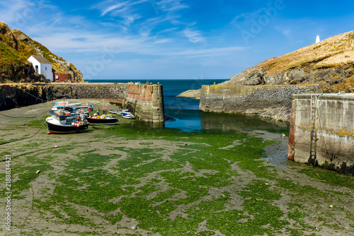 Foto Small boats resting on seaweed-covered harbor mud at low tide, historic stone qu