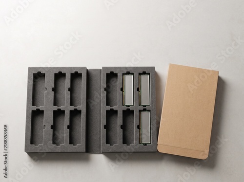 Open foam packaging inserts with slots, one holding reflective rectangular objects, next to a brown cardboard box on a light surface.