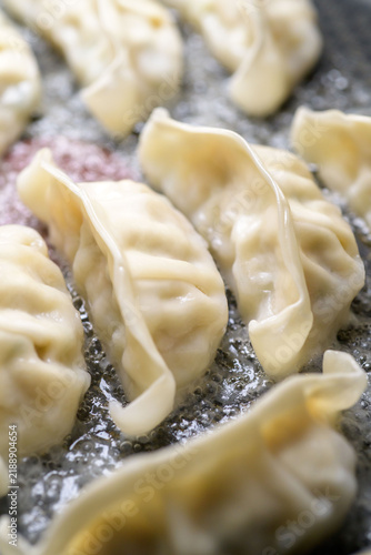 Crispy pan-fried dumplings cooking in hot oil with steam rising from the pan