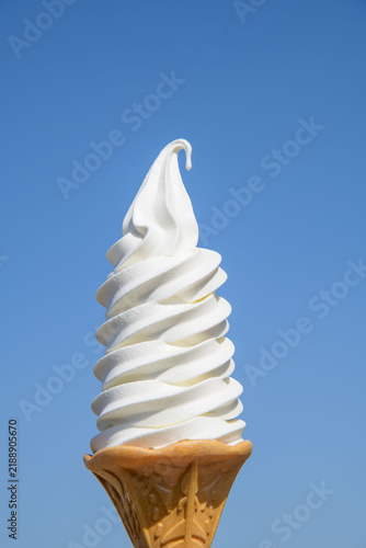 Soft serve ice cream cone against clear blue sky, refreshing summer dessert