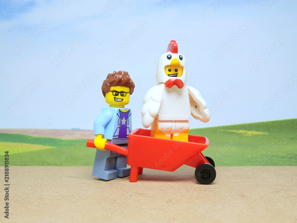 Fototapeta premium Indonesia - January 4, 2026 : Mini toy of action figure at outdoor with blur background. Miniature photography concept design. Minifigure of farmer with chicken at red wheelbarrow. Agriculture theme.