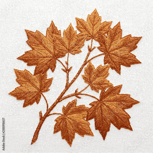 A detailed brown embroidered branch with autumn maple leaves on a white linen fabric background with intricate embroidery autumn