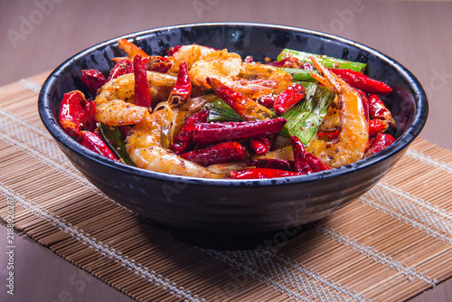 Delicious shrimp stir fry with red chili peppers and vegetables on a wooden table