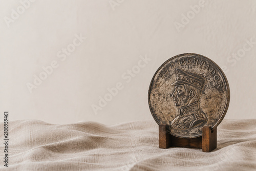 Weathered antique coin on wooden stand over linen fabric, history and heritage concept