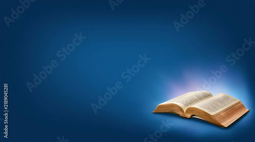 Open holy bible glowing with divine light on dark blue background representing faith and spirituality.