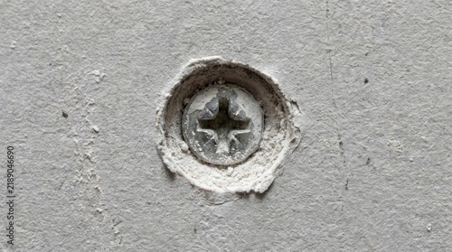 Close-up of metal phillips screw in concrete wall.