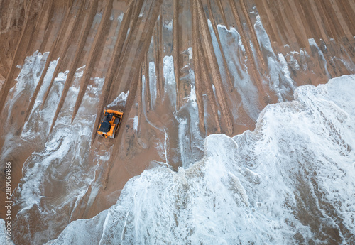 Canvastavla A tracked earthmover works along a wet sandy shoreline as ocean waves wash across freshly graded sections of beach