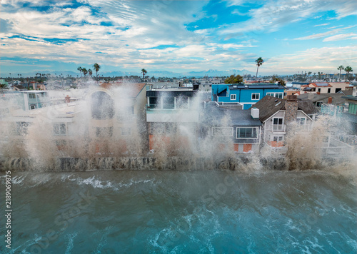 Large waves crash against oceanfront homes during heavy surf, sending spray above seawalls and highlighting the risks of coastal flooding and erosion