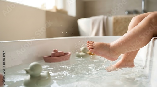 Cute baby feet splashing in a warm bathtub filled with water and floating toys during evening routine
