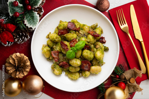 Delicious Italian gnocchi with pistachio pesto and fried bacon. Top-down view of the table. Christmas meal with a festively decorated table.